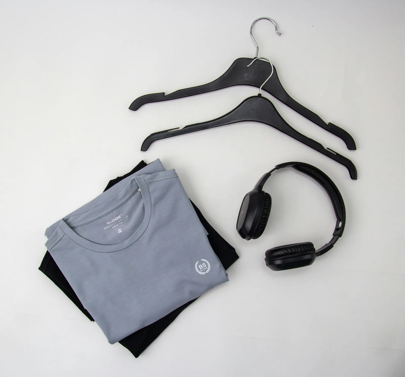 Camiseta gris doblada junto a unas perchas negras y unos auriculares