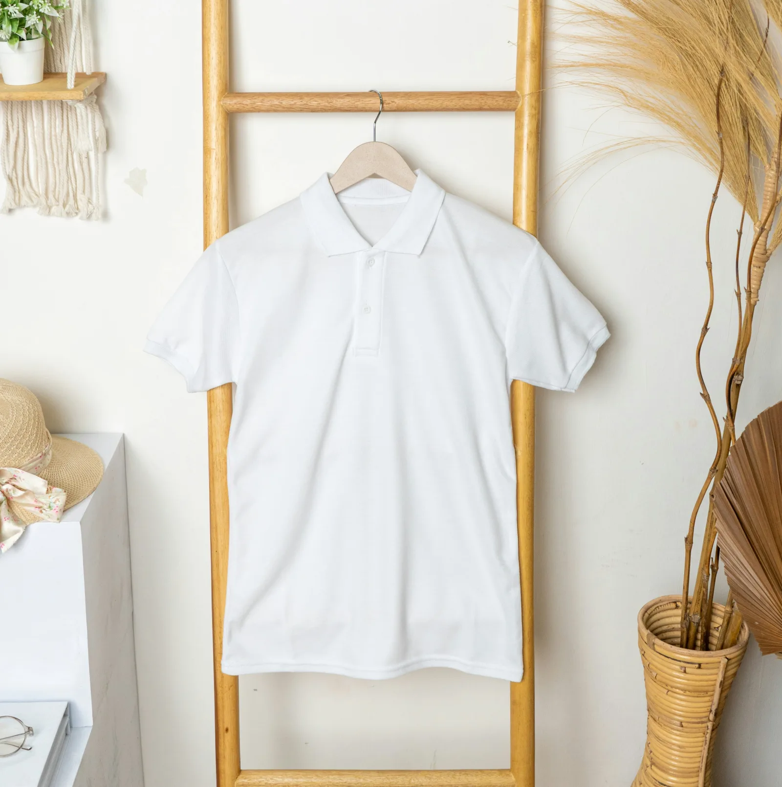 Polo blanco colgado de una percha de madera junto a una planta