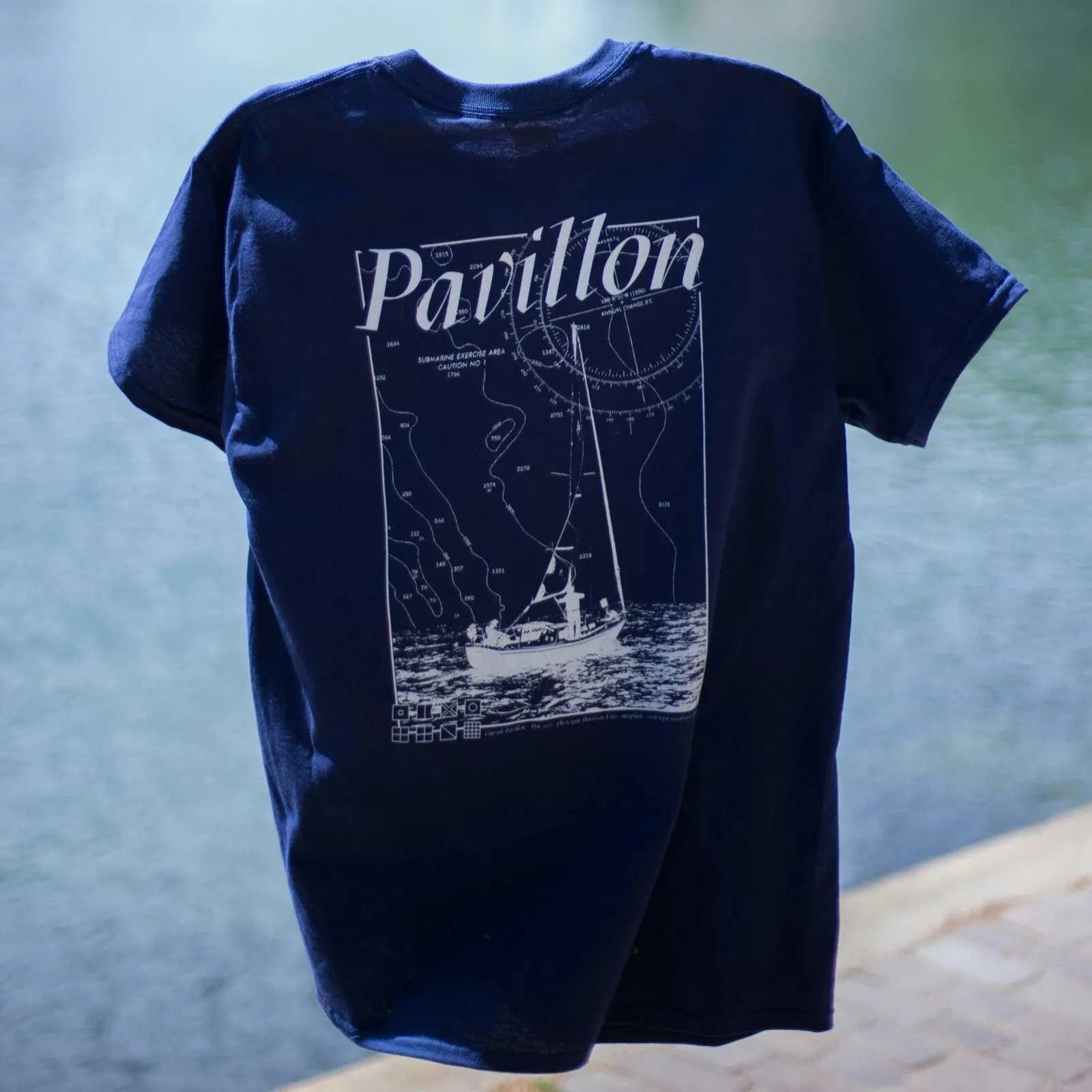 Camiseta azul marino con la serigrafía de un velero, extendida sobre una superficie azul