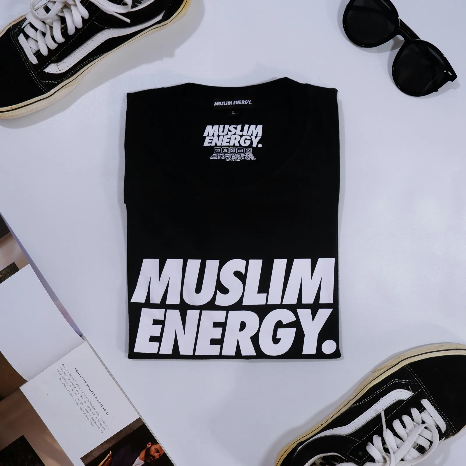 Camiseta negra doblada sobre fondo claro, entre unas gafas de sol y unas zapatillas